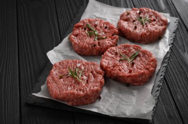 Kasap tahtasına çiğ sığır burger köftesi, biberiye ve biber. Siyah arka plan. Yukarıdan görüntüle.