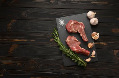 Siyah ahşap arka planda çiğ kovboy bifteği ve baharatları. BBQ Top Manzarası. Metin için boş alan.