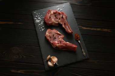 Siyah ahşap arka planda çiğ kovboy bifteği ve baharatları. BBQ Top Manzarası. Metin için boş alan.