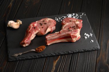 Siyah ahşap arka planda çiğ kovboy bifteği ve baharatları. BBQ Top Manzarası. Metin için boş alan.