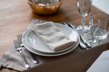 Gümüş takımlar, gri peçete ve bej ipek masa örtüsü üzerine beyaz çanak çömlek.