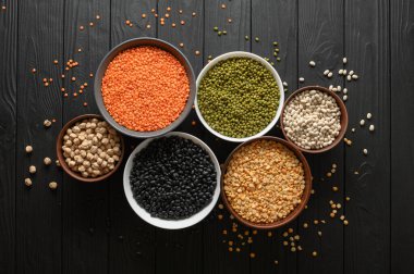 Koyu ahşap bir masa üzerinde çeşitli ham baklagiller.