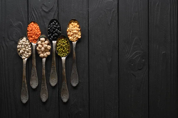 Siyah ahşap arka planda eski gümüş kaşıklardaki baklagillerin çeşitliliği.