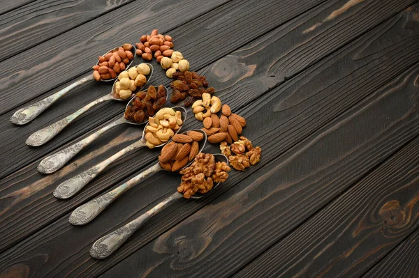 Hazelnut, cashews, raisins, almonds, peanuts, walnuts in silver spoons on a rustic background