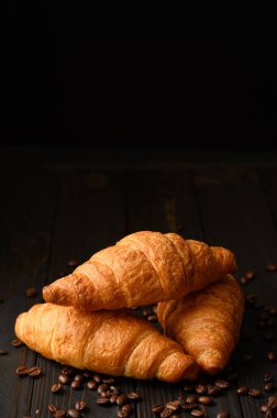 Ahşap zemin üzerinde kahve çekirdekleri olan kruvasanlar..