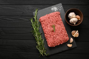 Tahta kesme tahtasındaki taze çiğ et ya da tavuk eti kekik, baharat ve sarımsaklı. Siyah ahşap arka plan. Üst Manzara. Boşluğu kopyala.