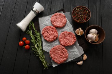 Kasap tahtasına çiğ sığır burger köftesi, biberiye ve biber. Siyah arka plan. Yukarıdan görüntüle.