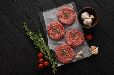Kasap tahtasına çiğ sığır burger köftesi, biberiye ve biber. Siyah arka plan. Yukarıdan görüntüle.