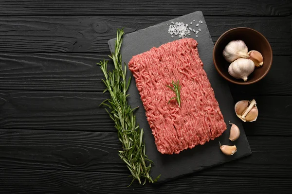 Tahta kesme tahtasındaki taze çiğ et ya da tavuk eti kekik, baharat ve sarımsaklı. Siyah ahşap arka plan. Üst Manzara. Boşluğu kopyala.
