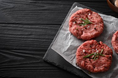 Kasap tahtasına çiğ sığır burger köftesi, biberiye ve biber. Siyah arka plan. Yukarıdan görüntüle.