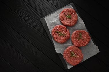 Kasap tahtasına çiğ sığır burger köftesi, biberiye ve biber. Siyah arka plan. Yukarıdan görüntüle.