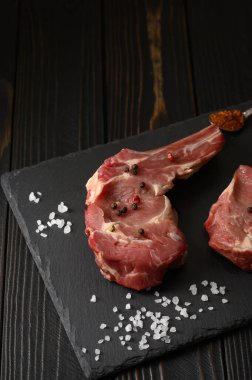 Siyah ahşap arka planda çiğ kovboy bifteği ve baharatları. BBQ Top Manzarası. Metin için boş alan.