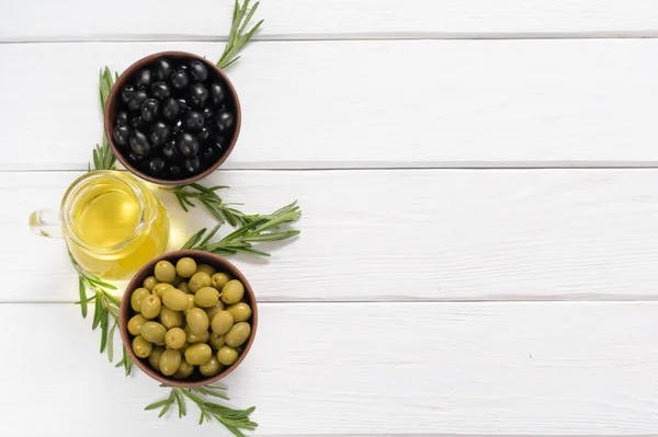 Black and green olives on a white wooden background.