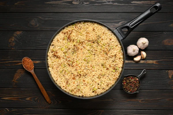 Fried rice with onions and zucchini in a pan on a rustic wooden background.