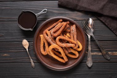 Homemade churros with chocolate on a dark wooden rustic background.
