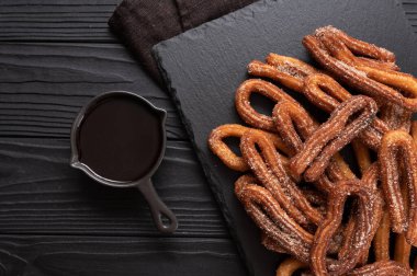 Homemade churros with chocolate on a dark wooden rustic background.