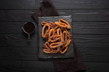 Homemade churros with chocolate on a dark wooden rustic background.
