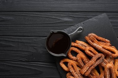 Homemade churros with chocolate on a dark wooden rustic background.