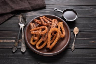 Homemade churros with chocolate on a dark wooden rustic background.