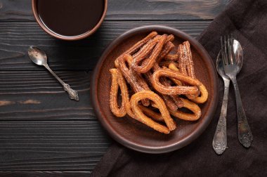 Homemade churros with chocolate on a dark wooden rustic background.
