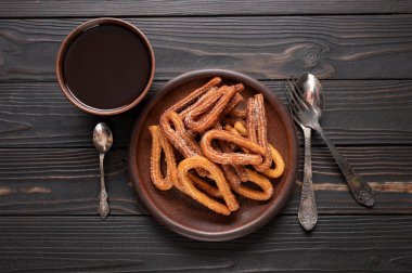 Homemade churros with chocolate on a dark wooden rustic background.
