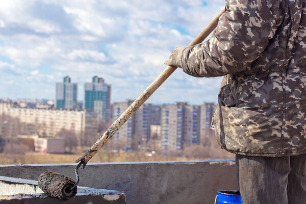 Roofer worker painting black coal tar or bitumen at concrete surface by the roller brush