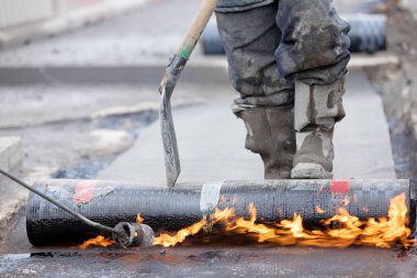 Su yalıtımı işi. SBS modifiye edilmiş Bitumen rulo çarşafını Butane Gaz Üfleme Meşalesi ile beton köprü güvertesine uygulayan inşaat işçisi.