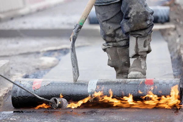 Su yalıtımı işi. SBS modifiye edilmiş Bitumen rulo çarşafını Butane Gaz Üfleme Meşalesi ile beton köprü güvertesine uygulayan inşaat işçisi.