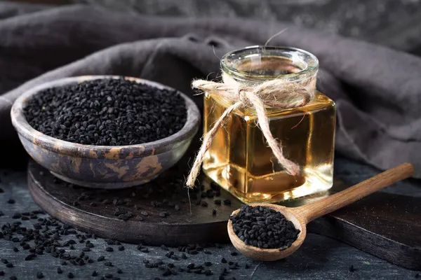 碗中的黑种子和黑色背景上的油 — 图库照片