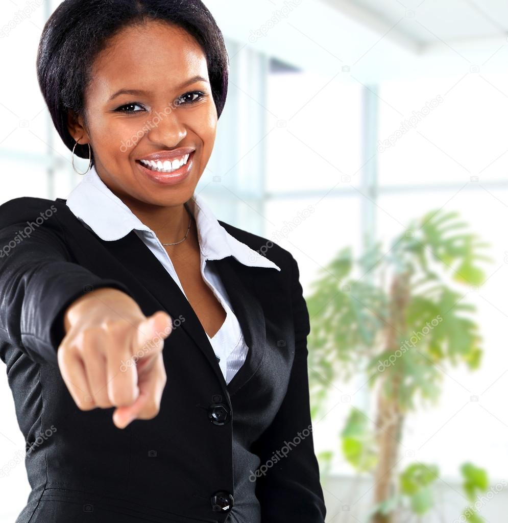 Smiling black business woman pointing on camera in office