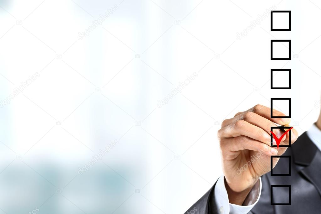Young businessman checking mark on checklist with marker. Isolated on white.