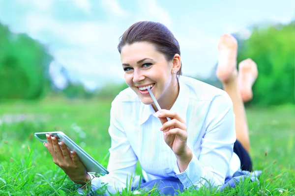 Tablet çimenlerin üzerinde döşeme açık kullanan genç kadın gülümsüyor. — Stok fotoğraf