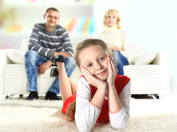 Un retrato de una chica acostada en el suelo y sonriendo con sus padres en el fondo —  Fotos de Stock