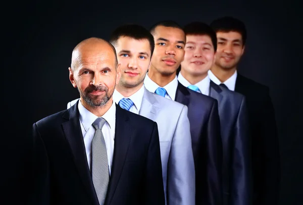 Business team formed of young businessmen and the leader standing over a dark background — Stock Photo, Image