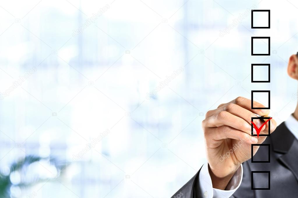 Young businessman checking mark on checklist with marker.