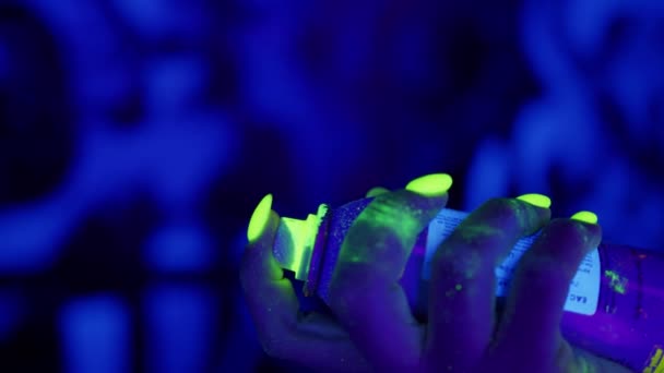 Neon brilhante UV make-up spray aerossol voando para fora com mulher dedo pressionando pode tampão tiro no fundo ultravioleta — Vídeo de Stock