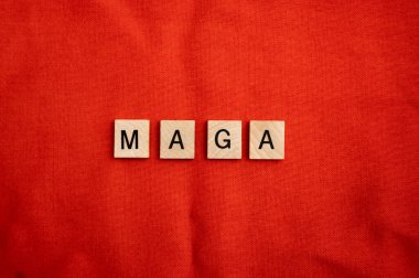 Kırmızı zemin üzerinde tahta döşeme harfleri olan MAGA kavramı.