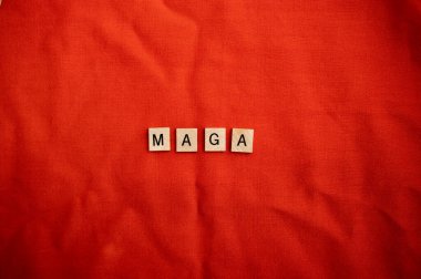 Kırmızı zemin üzerinde tahta döşeme harfleri olan MAGA kavramı.