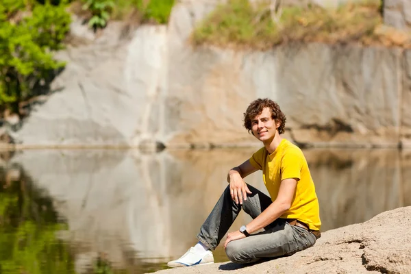 一个年轻人坐在湖畔上 — 图库照片