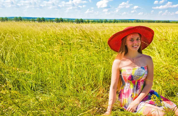 Beautiful girl in a red hat sitting in a field — Stock Photo, Image