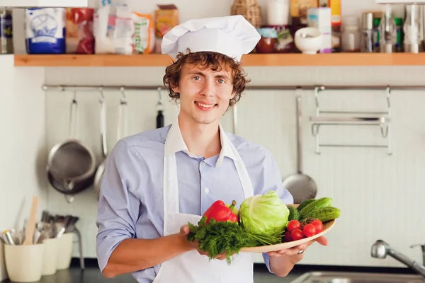 Chef amistoso preparando verduras en su cocina — Foto de Stock