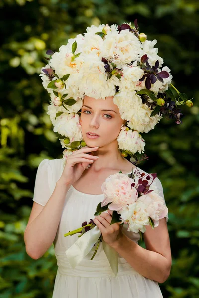 Schönes junges Mädchen mit einer Mütze voller Blumen auf dem Kopf — Stockfoto