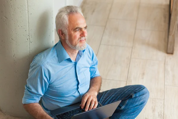 Oude man met laptop zittend op de vloer — Stockfoto