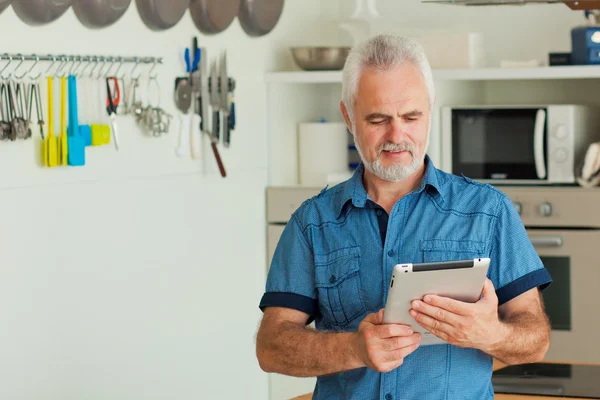 Oude man met tablet achter de keuken — Stockfoto