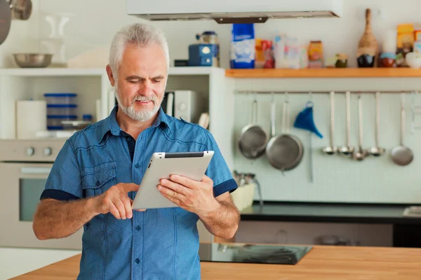 Hombre viejo con la tableta sentada en la cocina — Foto de Stock