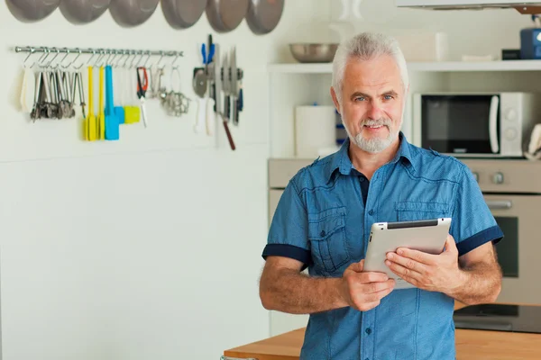 Starý muž s tabletem sedí v kuchyni — Stock fotografie