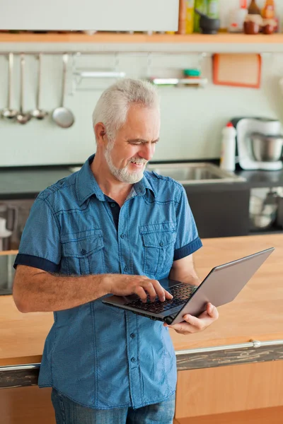Oude man met laptop in de keuken — Stockfoto