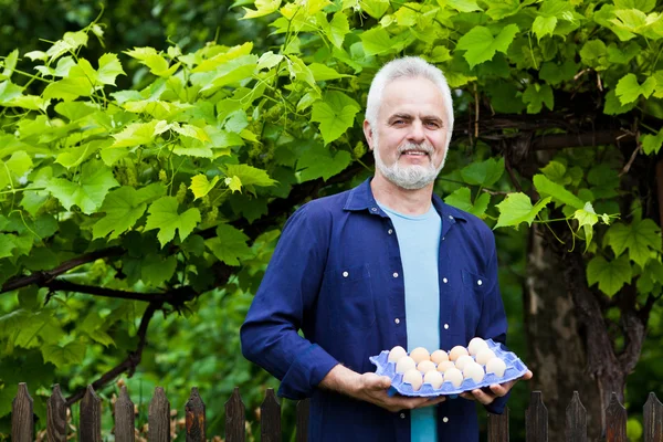 Happy young man holding his chicken and basket of eggs in his ga — Stock Photo, Image