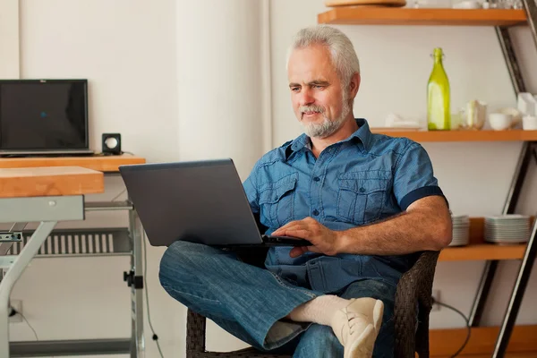 Äldre man med anteckningsboken sitter på köket — Stockfoto