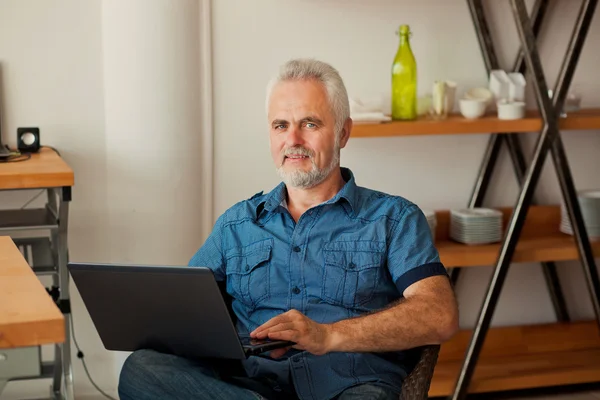Senior man with notebook sitting at the kitchen — Stock Photo, Image